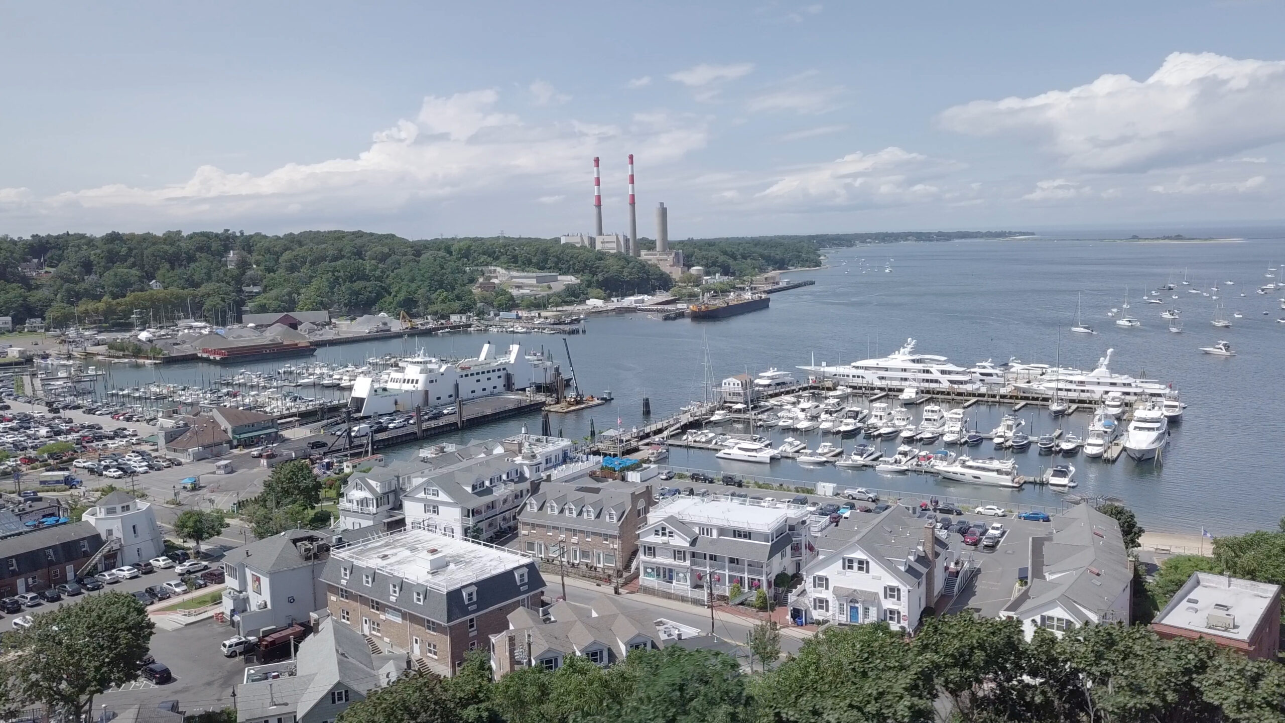 Aerial view of Port Jefferson Harbor in Long Island, New York with marina, boats, waterfront buildings, and shoreline along the coastal village.