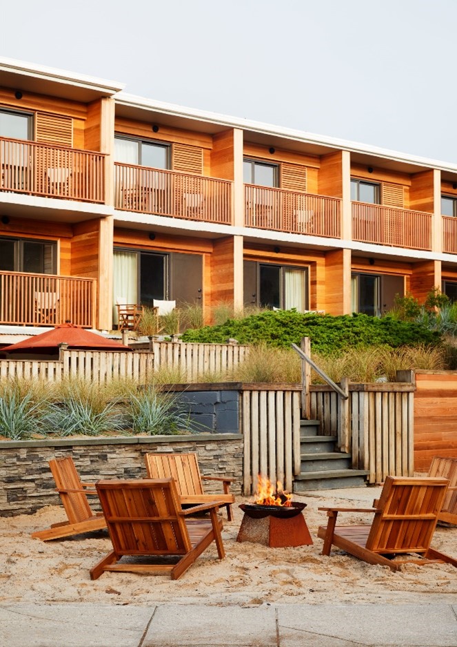 Marram rooms with wooden balconies, chairs, and tables overlooking the beach firepit