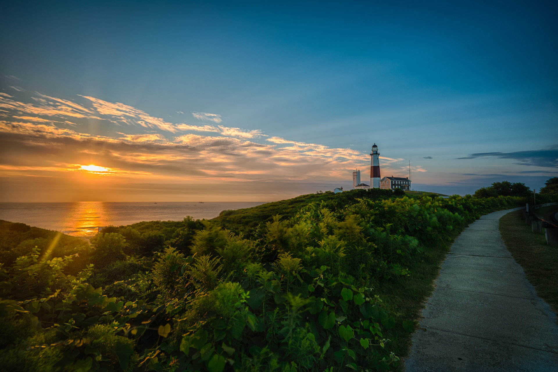 Montauk Point Lighthouse at sunset with greenery and ocean path