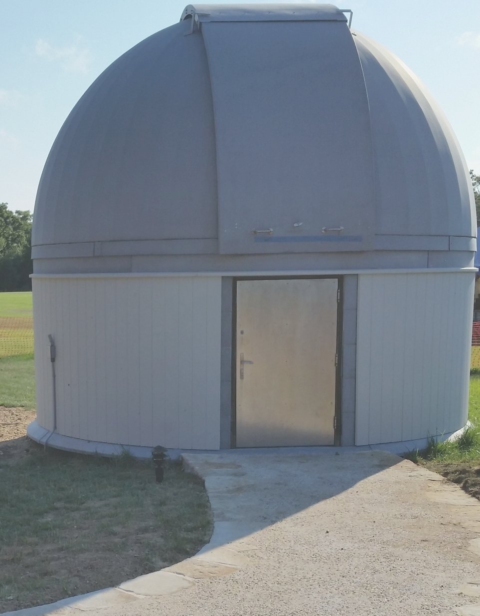 The silver dome-shaped Hamptons Observatory with a metallic door, surrounded by green grass and blue sky.
