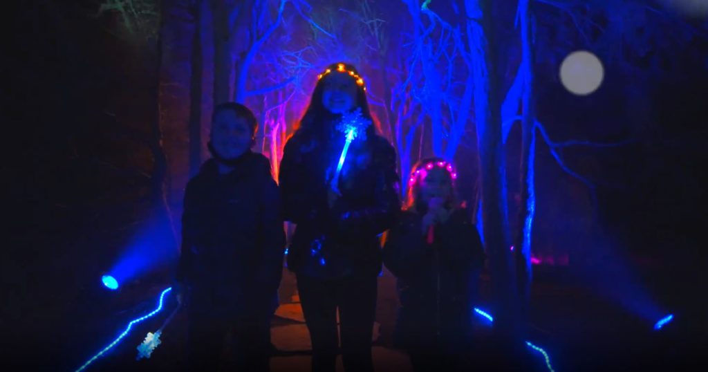 Image of three people facing the camera and looking above it in awe. The scene is washed in a glowing royal blue.