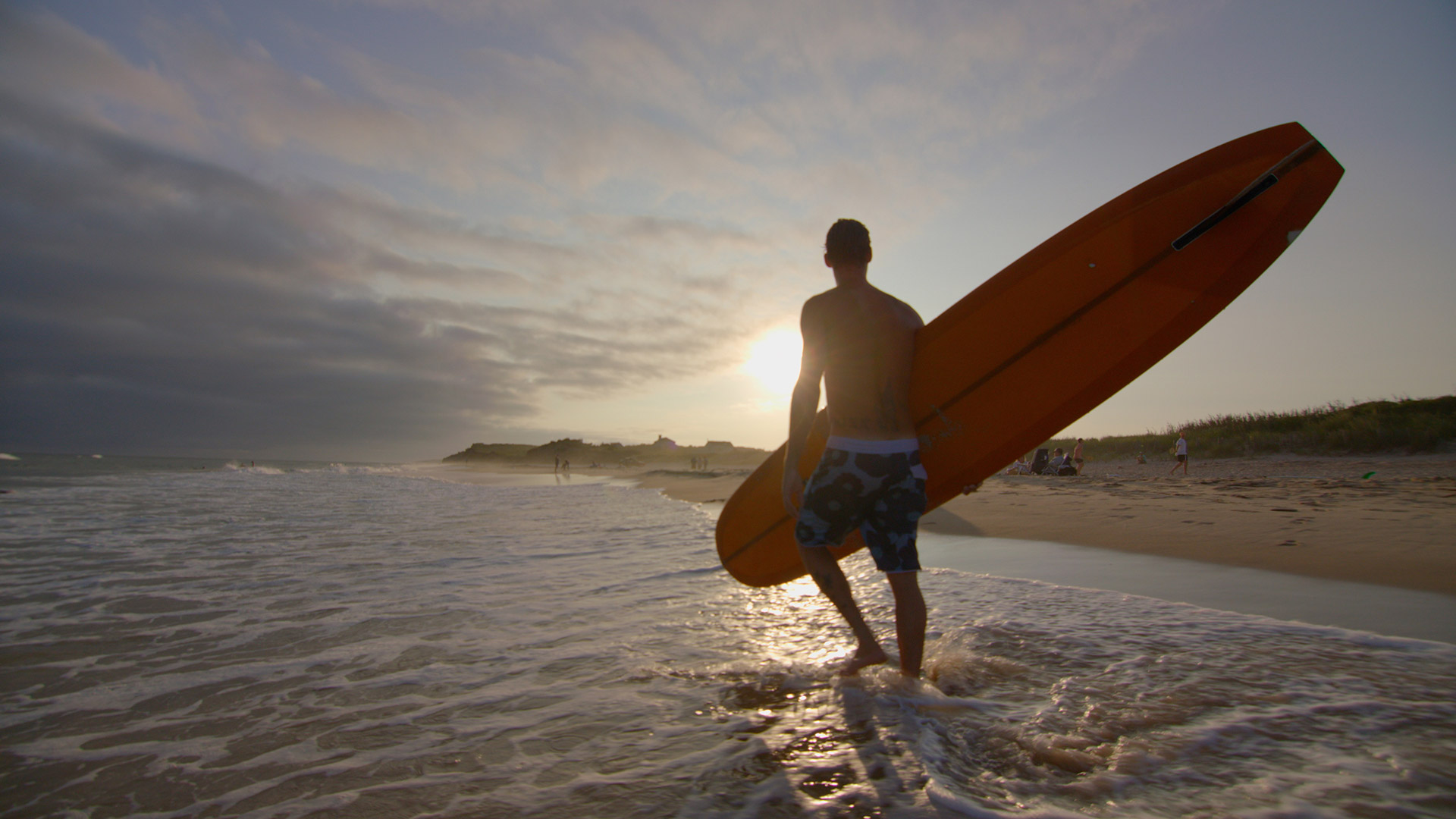 Surfer walking along the beach at sunrise on Long Island