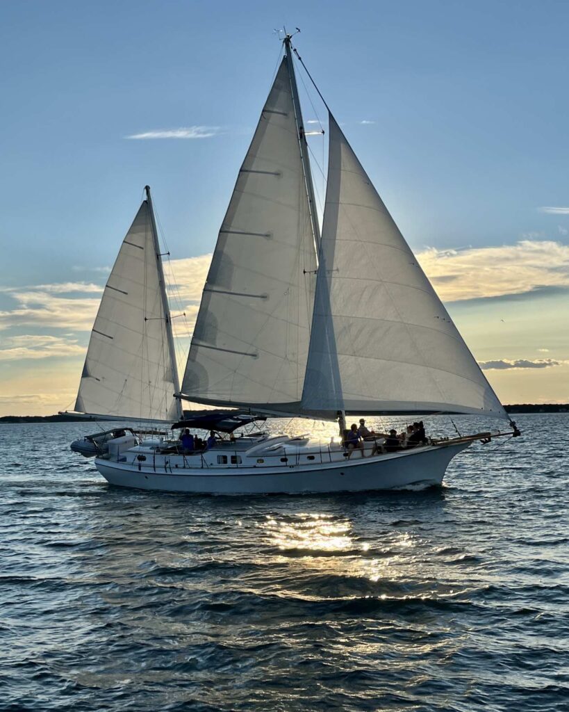 Sailboat with three sails centered on the open water during golden hour
