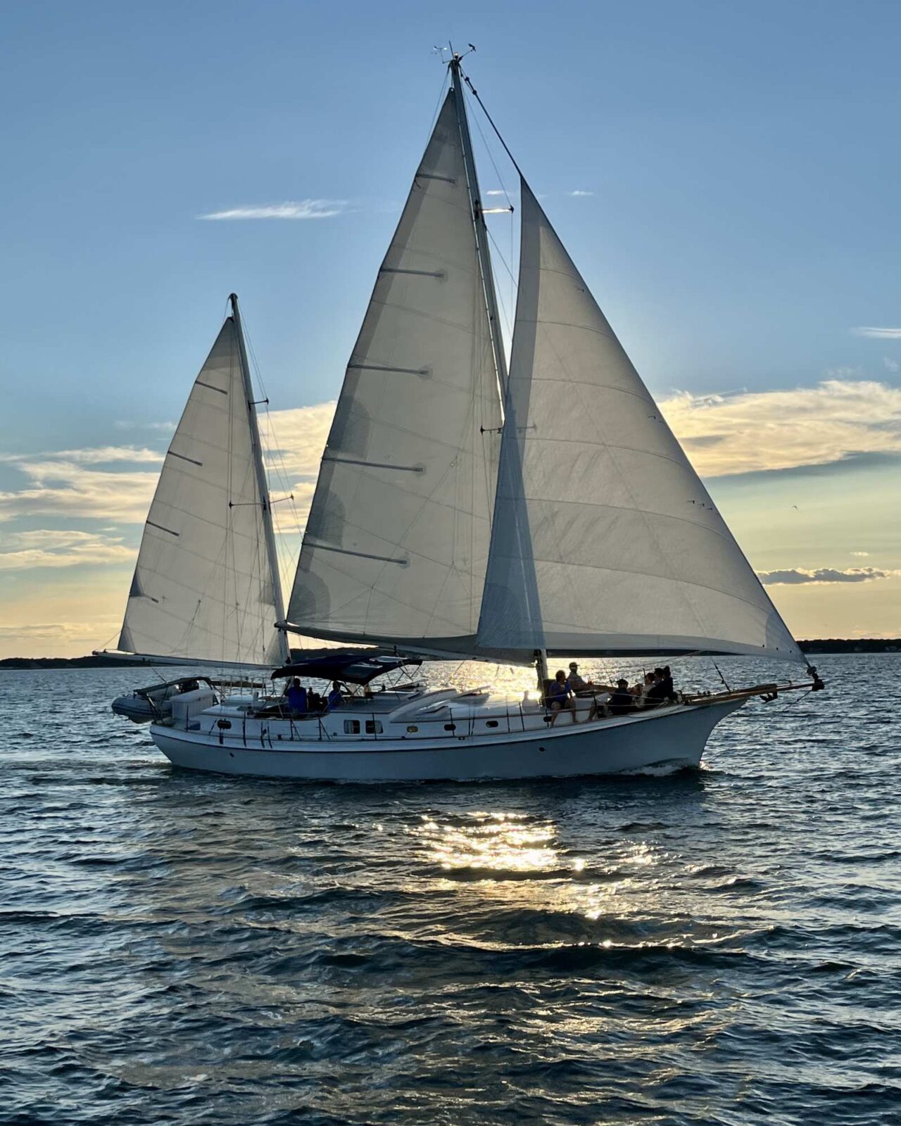 Sailboat with three sails centered on the open water during golden hour