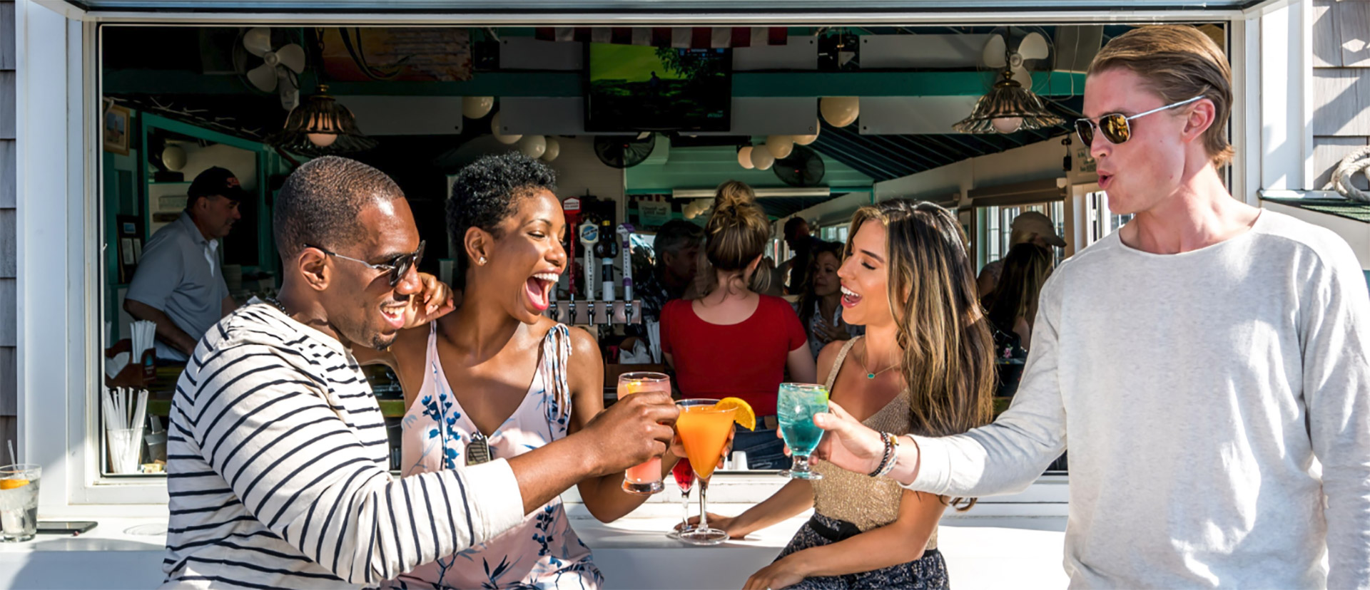 Friends toasting cocktails at an outdoor bar on Fire Island, Long Island