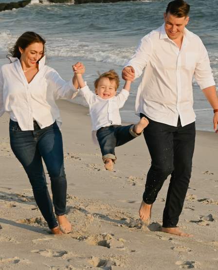 Mom and Dad lifting child up by their arms on the beach